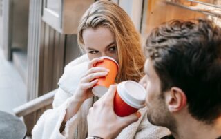 Young couple drinking hot beverages and looking at each other in cafe